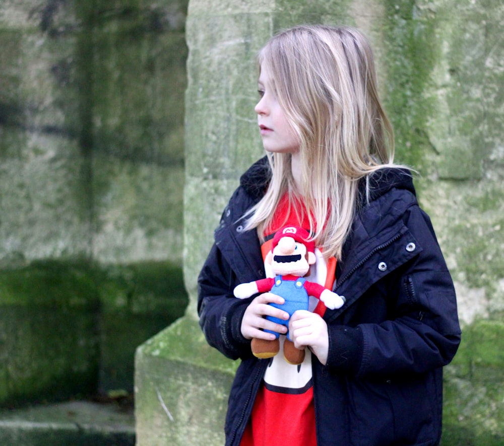 girl in black jacket holding red and white plush toy