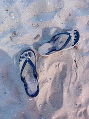 Pair of casual rubber flip-flops on a sandy beach background.