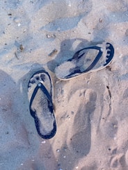 Colorful flip-flops lined up on sandy ground near a beach bonfire where people are sharing stories.