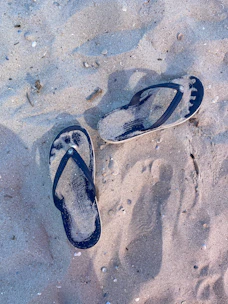 Pair of casual rubber flip-flops on a sandy beach background.