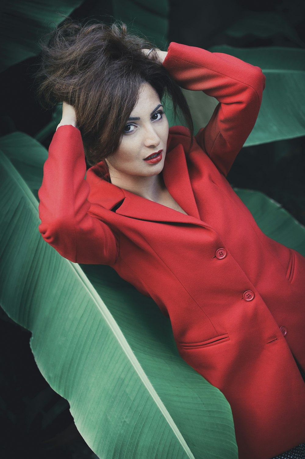 woman in red blazer leaning on green wooden wall