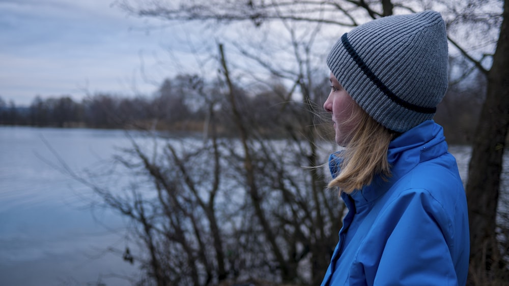 woman in blue jacket and gray knit cap looking at the lake