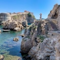 man standing on rock formation near body of water during daytime