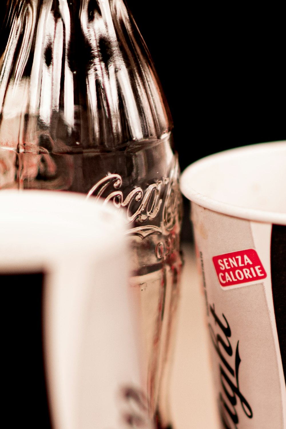 coca cola bottle beside white ceramic mug