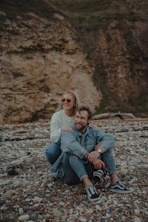woman in white sweater sitting beside man in blue denim jeans on rocky ground during daytime