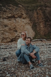 woman in white sweater sitting beside man in blue denim jeans on rocky ground during daytime