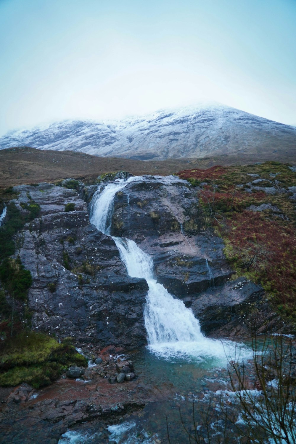 waterfalls near brown and green mountain under white sky during daytime