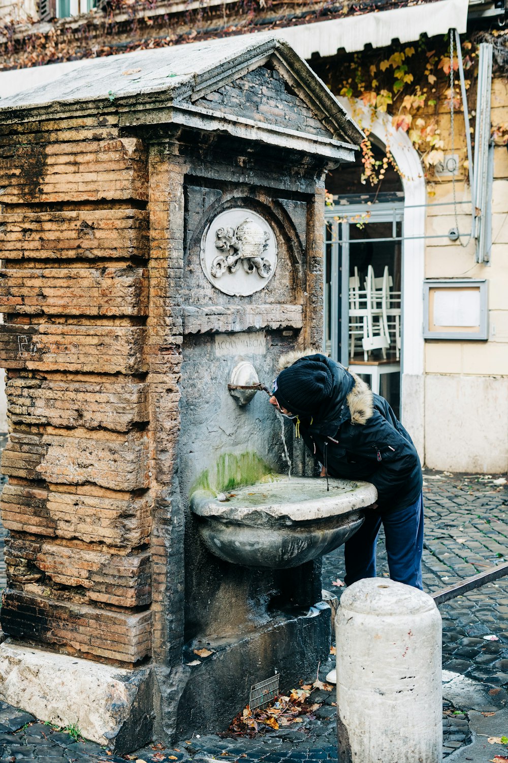 Mann in schwarzer Jacke gießt Wasser auf grauen Betonbrunnen