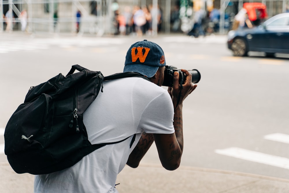 homem na camisa branca e mochila preta tirando foto usando a câmera dslr preta