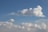 A close-up of fluffy white clouds drifting over a calm blue horizon.