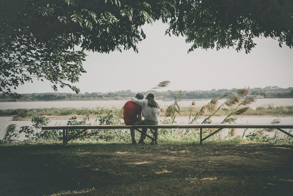 man in red shirt and black pants sitting on brown wooden bench