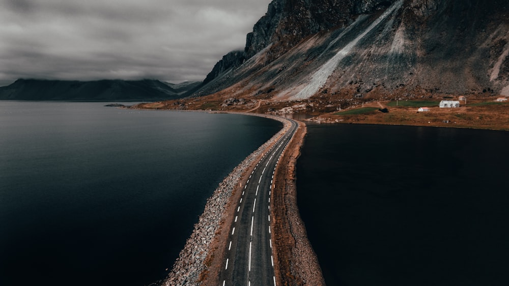 gray concrete road near body of water and mountain during daytime