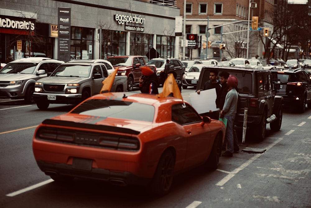 people riding red chevrolet camaro on road during daytime
