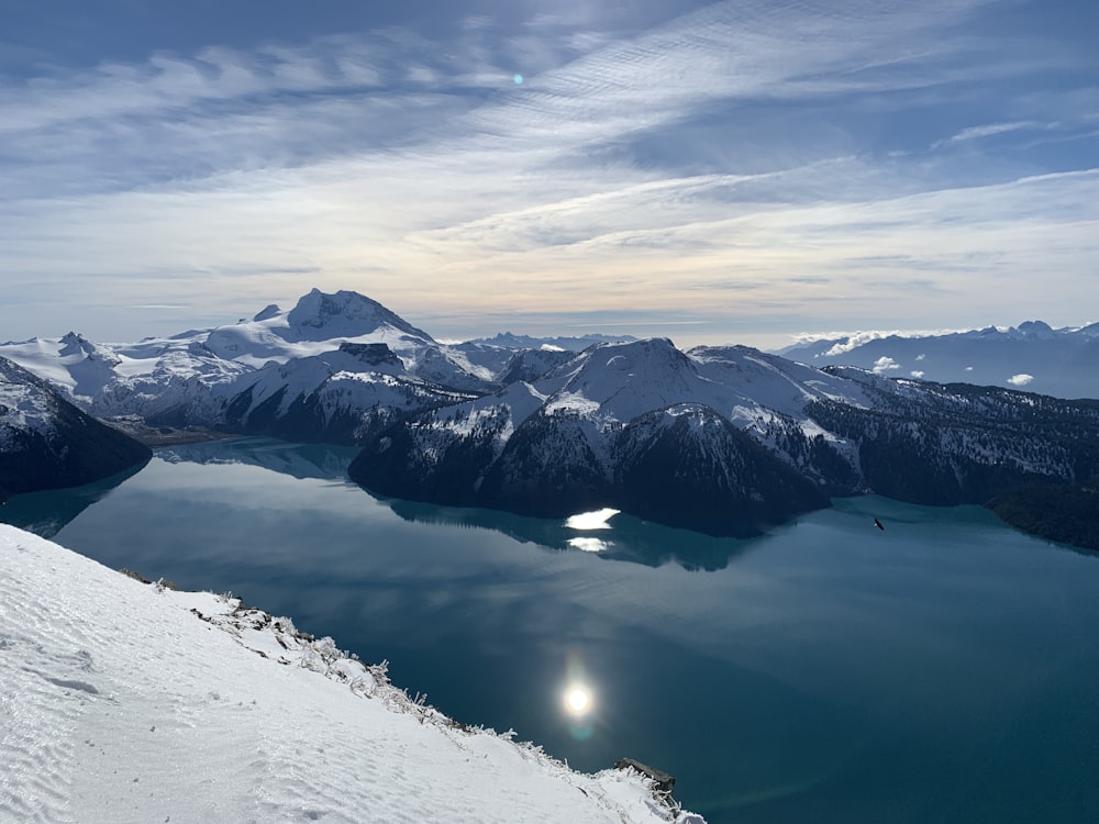 Schneebedeckter Berg in Seenähe tagsüber unter bewölktem Himmel