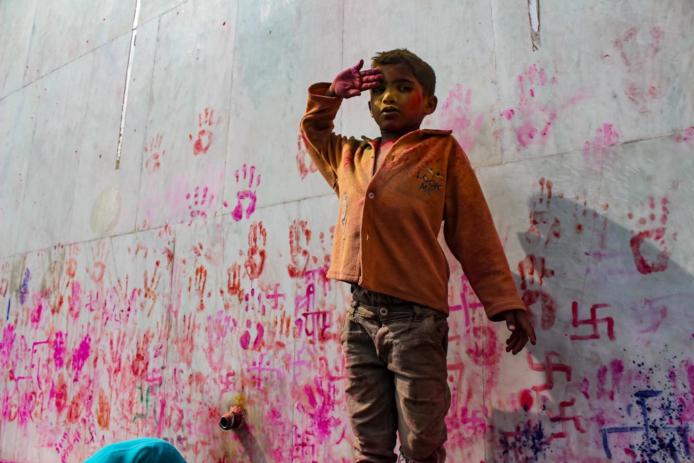 boy in brown button up shirt and blue denim jeans standing beside wall with graffiti