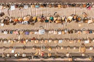 Numerous padlocks attached to a metal fence, each inscribed with different names, dates, or messages, symbolizing love or commitment.