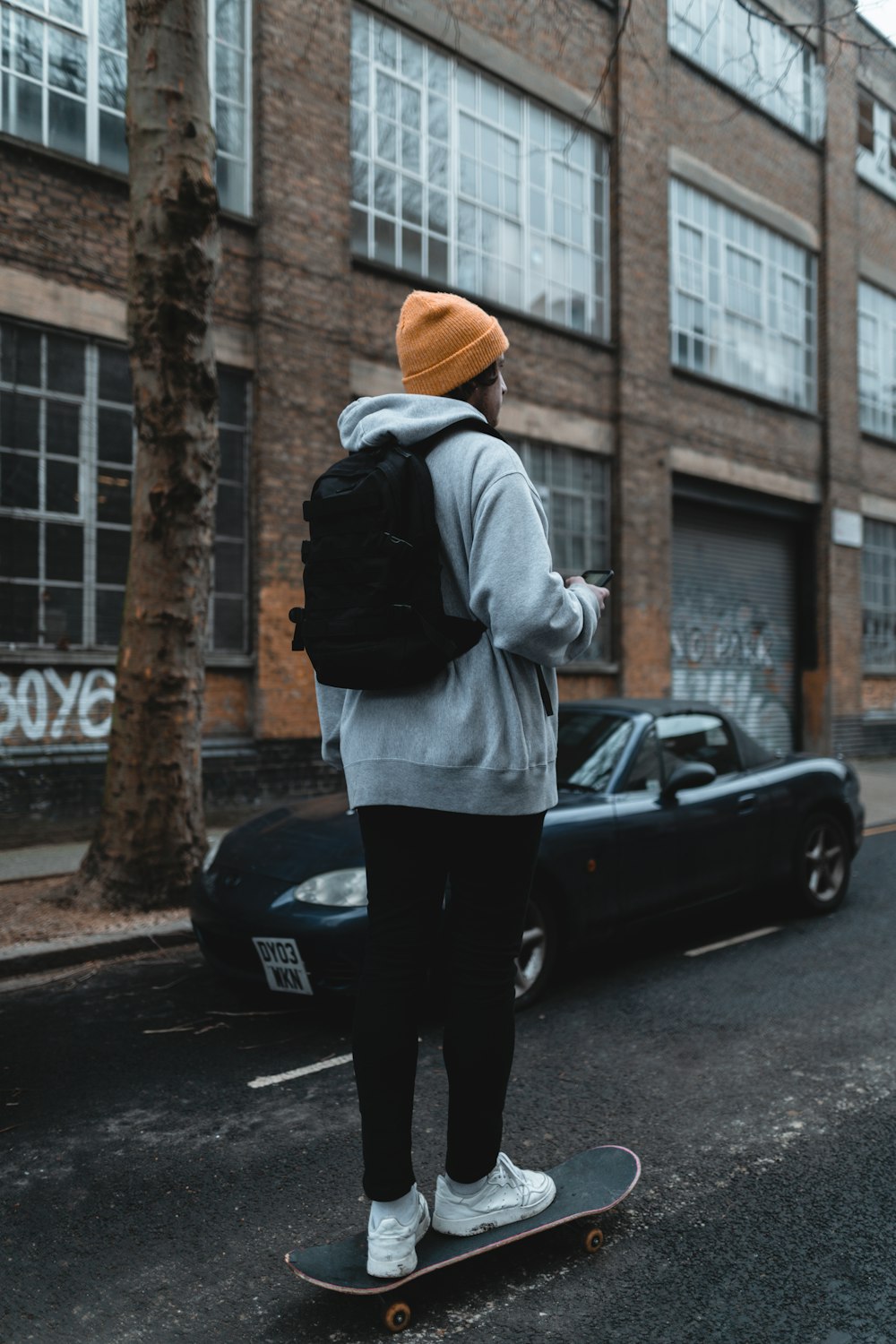 woman in gray hoodie and black pants standing beside black car during daytime