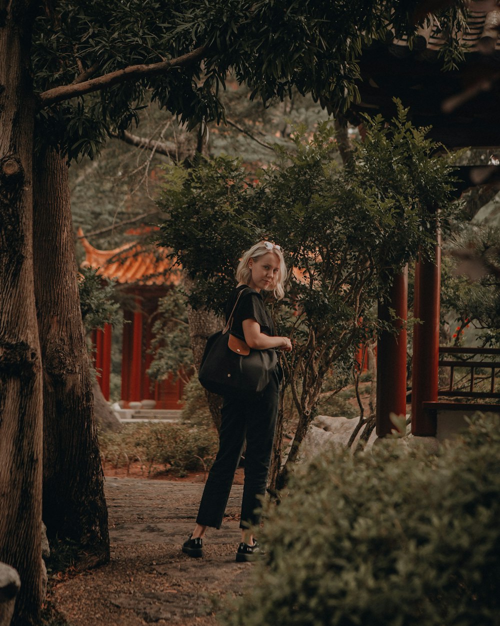 woman in black long sleeve shirt and black pants standing near green trees during daytime