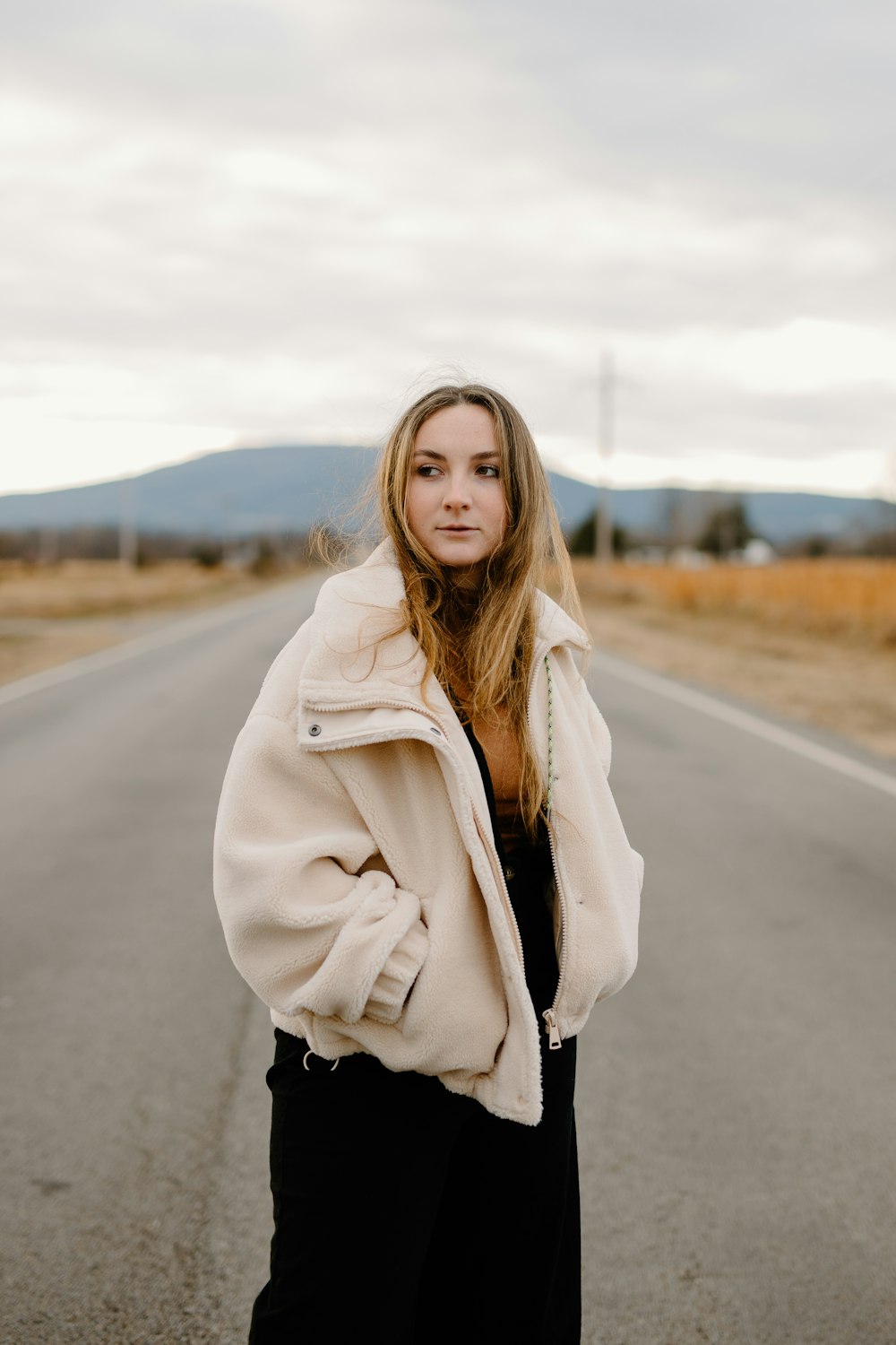 woman in white coat standing on road during daytime