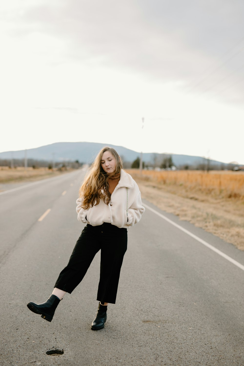 woman in white jacket and black pants standing on road during daytime