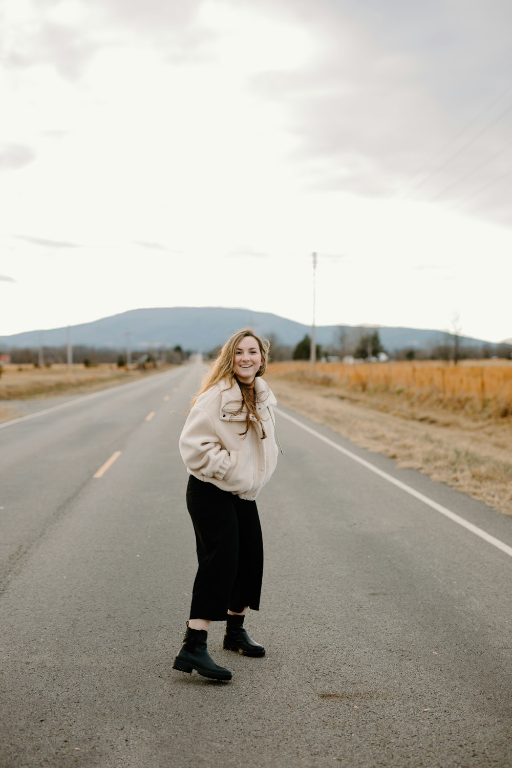 woman in white coat standing on road during daytime
