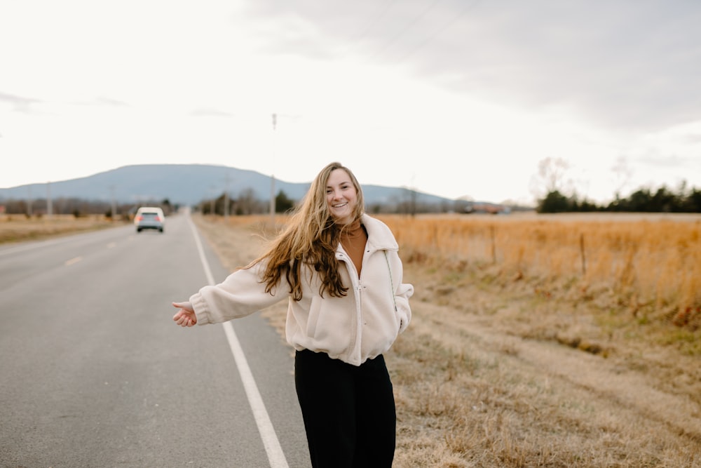 woman in white long sleeve shirt and black pants standing on road during daytime