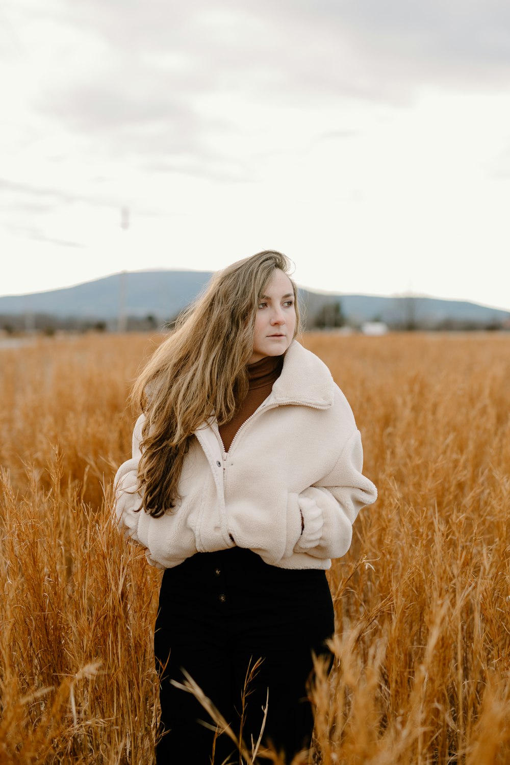 woman in white hoodie standing on brown grass field during daytime