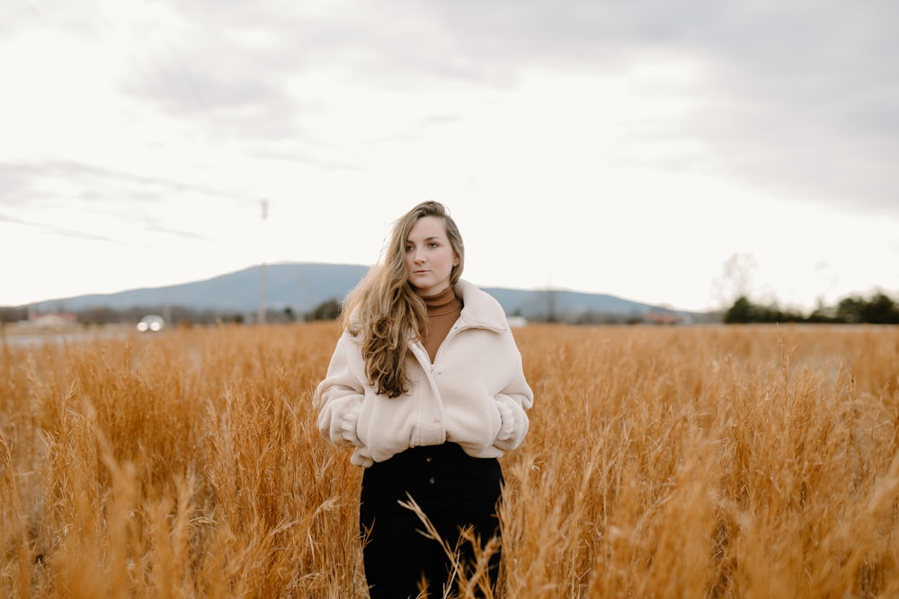 woman in white jacket standing on brown grass field during daytime