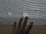 A hand is touching a mesh or netting material with a couple of holes in it. The background appears to be out of focus, showing a field or an outdoor area.