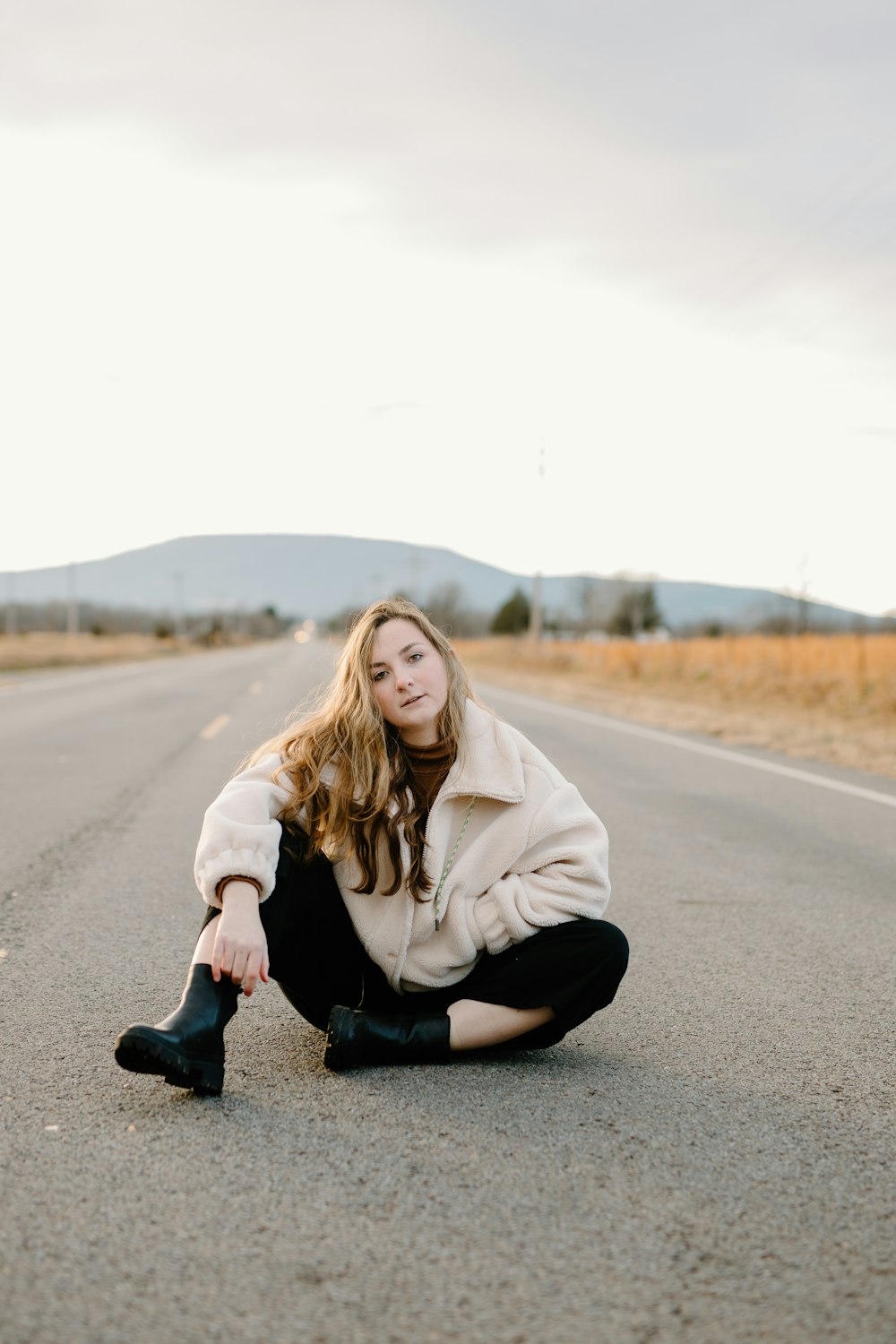 woman in white hoodie and black pants sitting on road during daytime