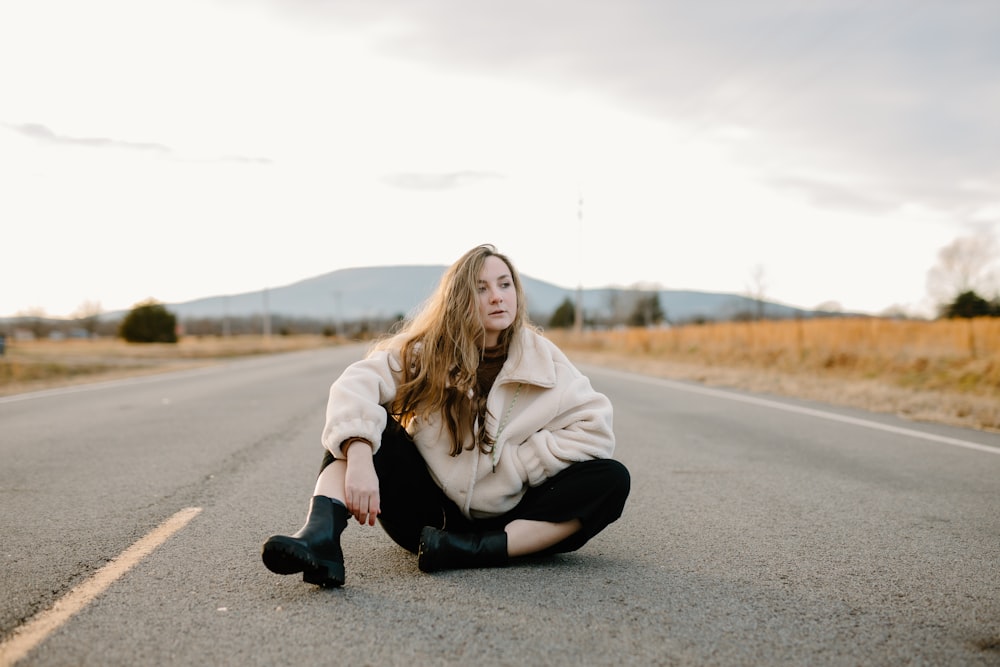 woman in white hoodie and black pants sitting on road during daytime