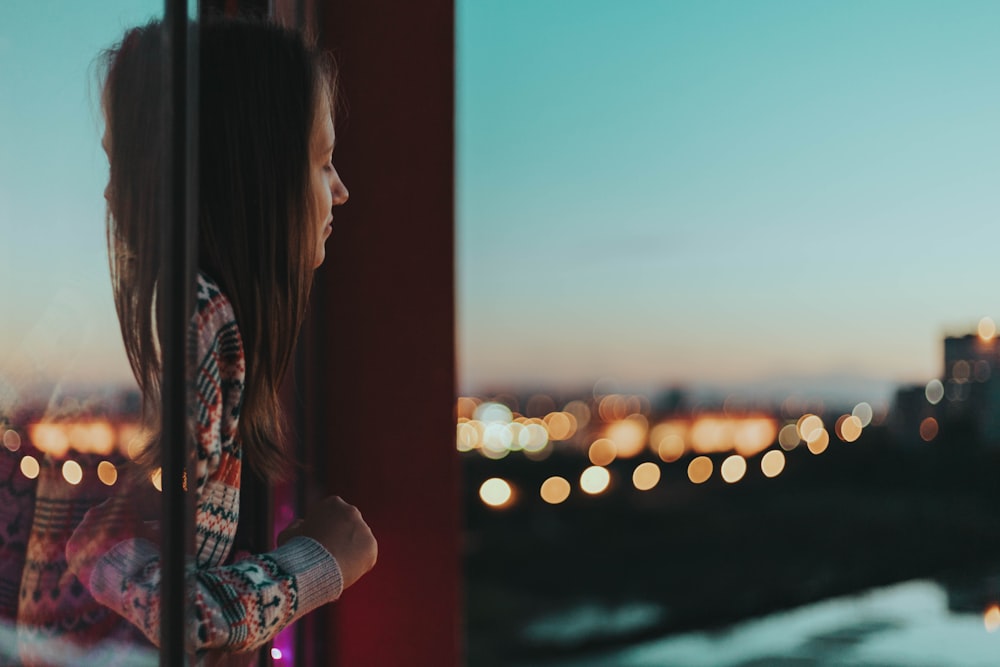 woman in red and blue floral long sleeve shirt standing near window during sunset