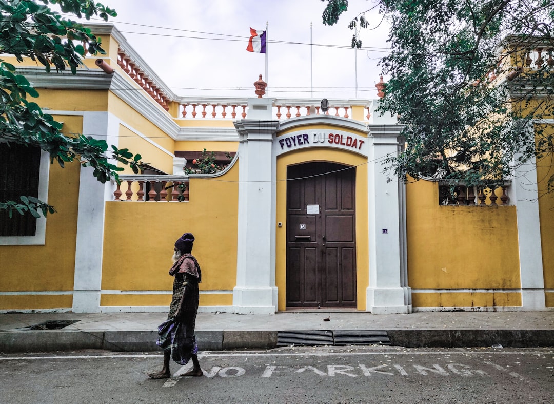 man in black jacket walking on sidewalk near yellow building during daytime