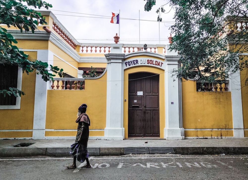 man in black jacket walking on sidewalk near yellow building during daytime