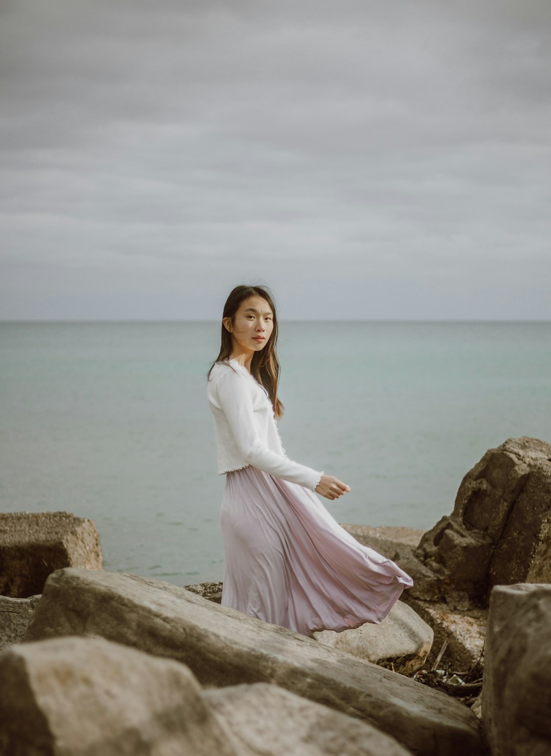 woman in white long sleeve dress sitting on brown rock near body of water during daytime