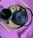 A black teapot and a black mug containing a dark liquid are placed on a woven tray with handles. There are waffle cookies broken into pieces in a small blue dish. The tray is positioned on a vibrant pink knit fabric.