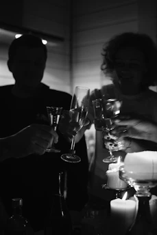 Guests raising glasses around a warmly lit table, with golden candlelight reflecting off dark wood surfaces.