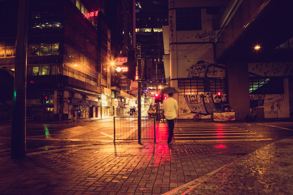 man in white shirt and red pants standing on sidewalk during night time