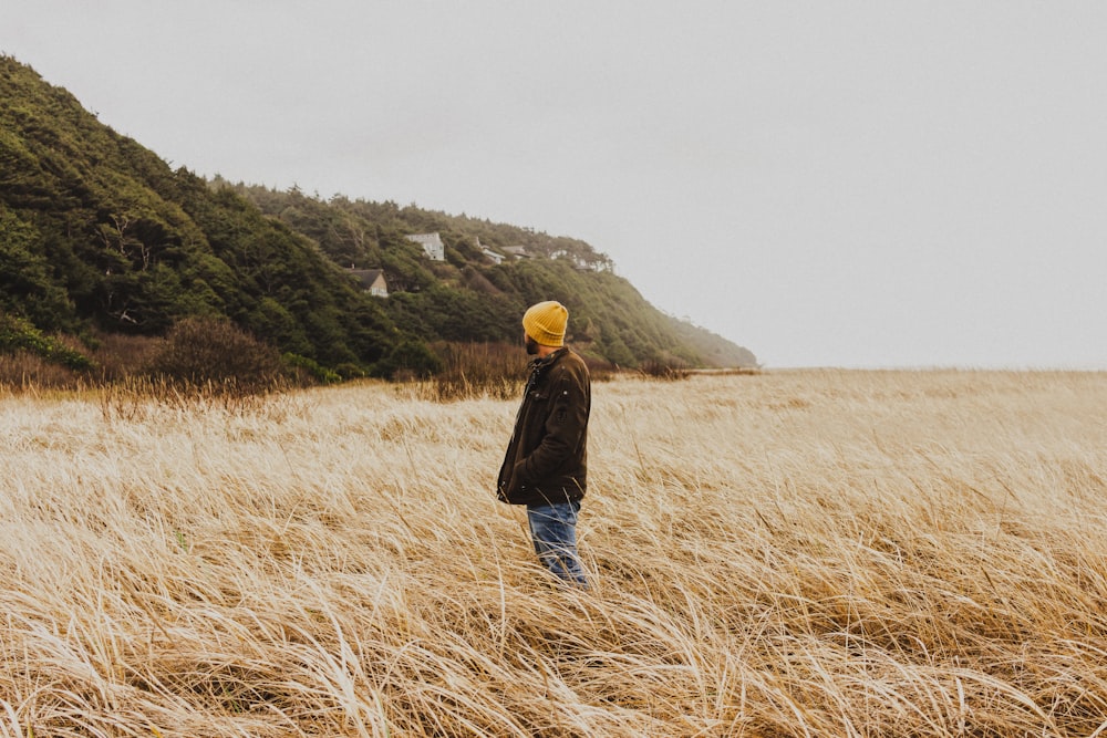 woman in black jacket and yellow knit cap standing on brown grass field during daytime