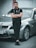 A man stands confidently with crossed arms in front of a silver BMW car. He is wearing black clothing including a jacket and pants. The car is parked on an urban street near a concrete wall, suggesting an outdoor setting.