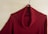 A red knit sweater with a cowl neck is hanging on a wooden hanger against a light wood grain background.