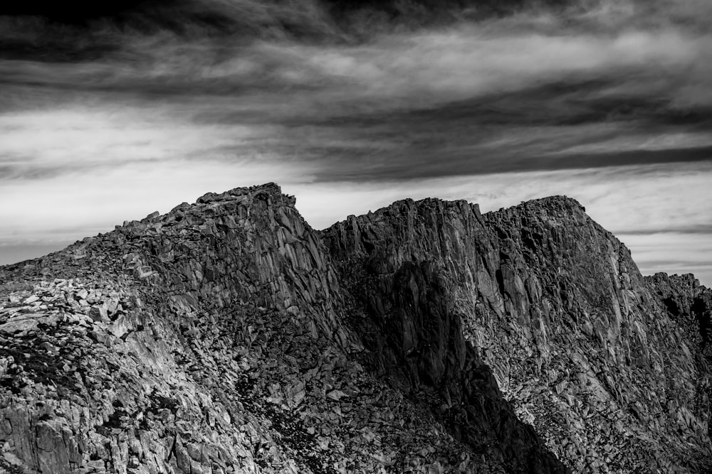 grayscale photo of rocky mountain under cloudy sky