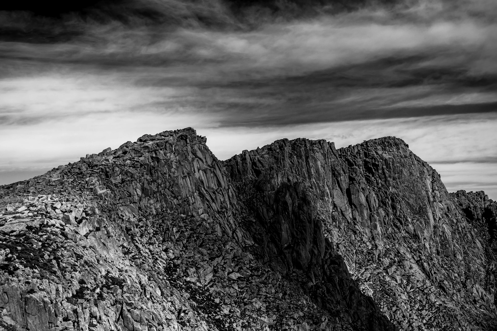 grayscale photo of rocky mountain under cloudy sky