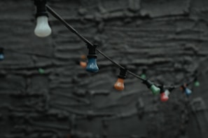 A cluster of colorful bulb lamps hanging at different heights against a neutral wall