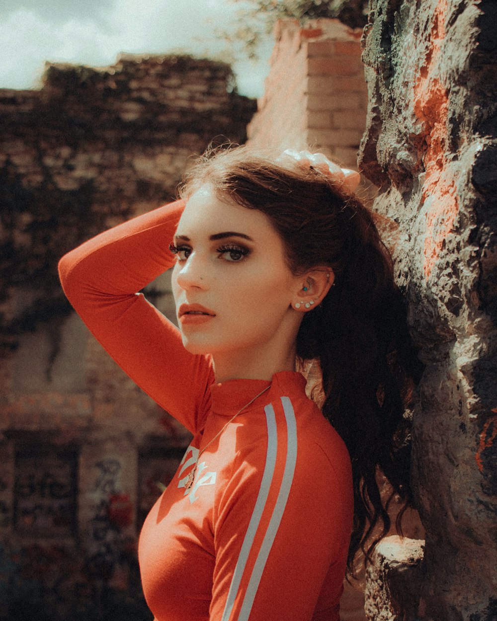 woman in red and white stripe polo shirt leaning on brown wall