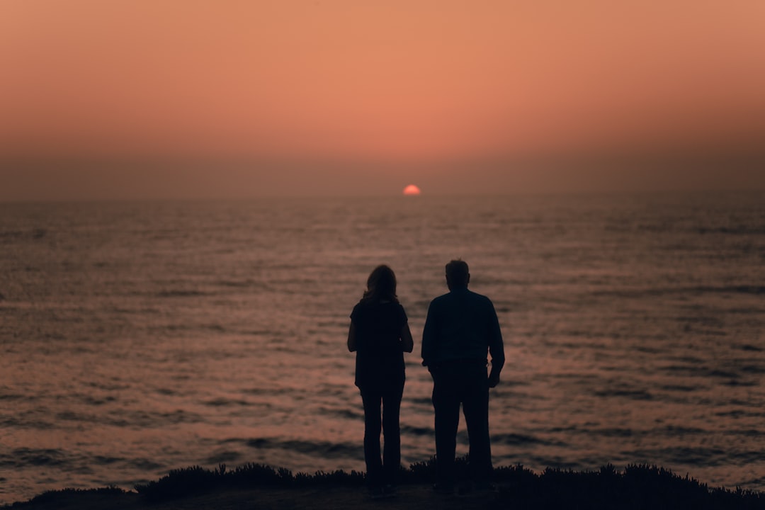 silhouette of 2 men standing on seashore during sunset