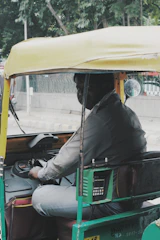 A technician installing a sleek auto fare meter inside a bright yellow auto rickshaw on a sunny city street.