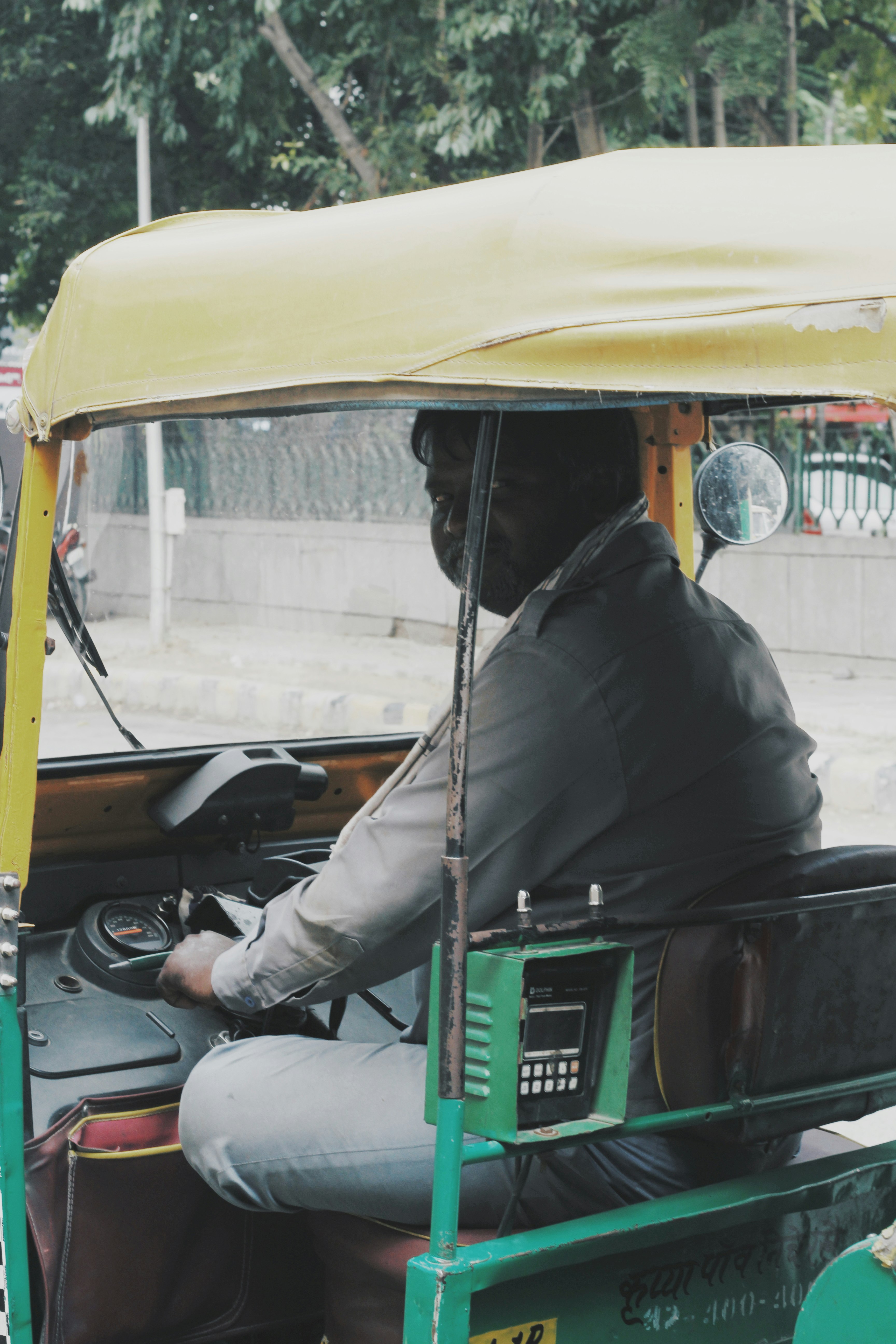 man in black jacket sitting on green and yellow auto rickshaw