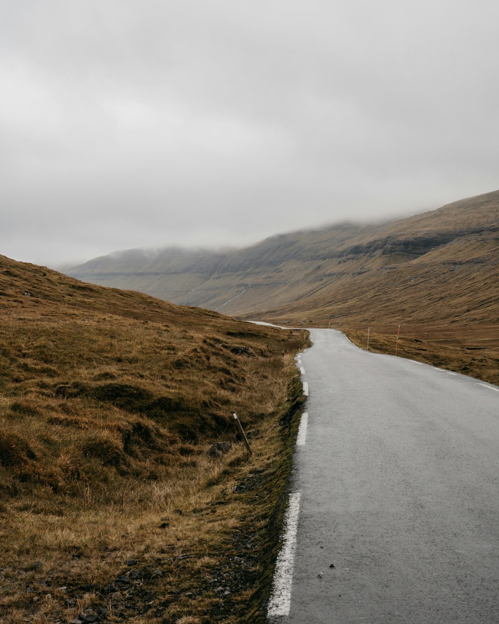 gray asphalt road near brown mountain under white sky during daytime