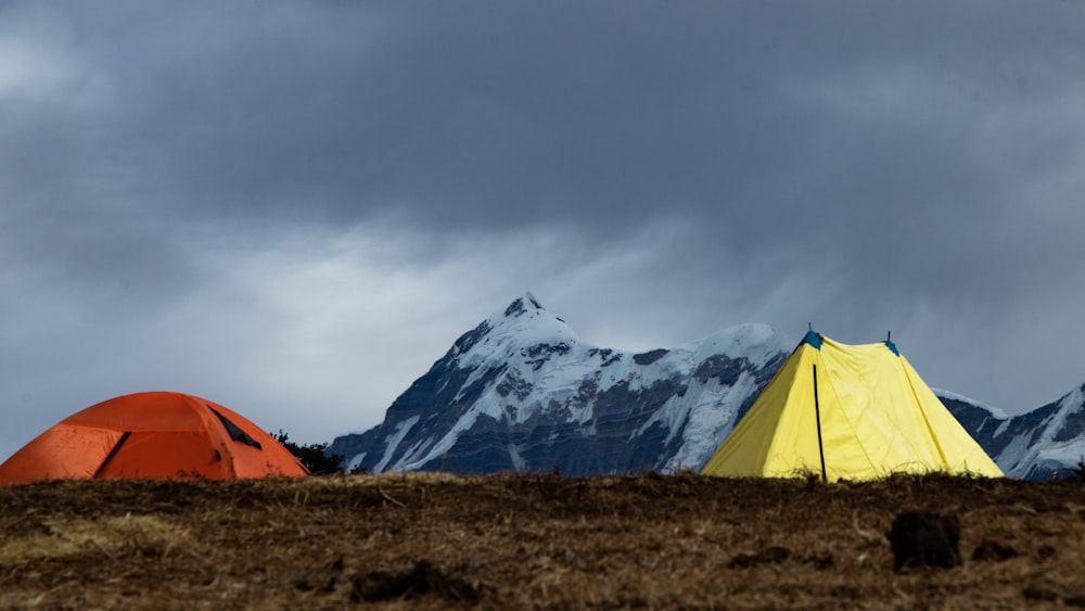 orange tent on brown grass field near snow covered mountain during daytime